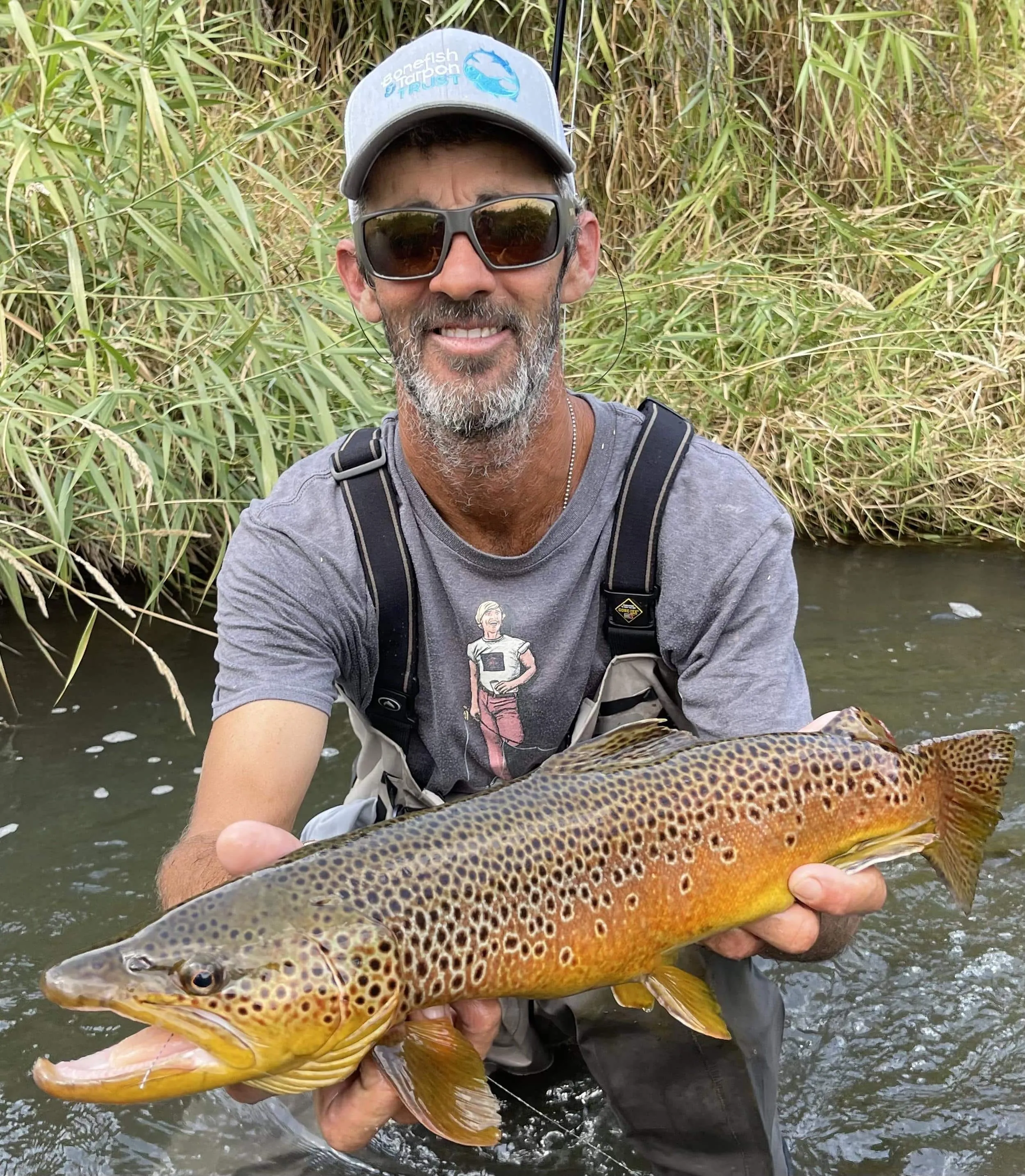 Captain David in a stream holding a large brown trout
